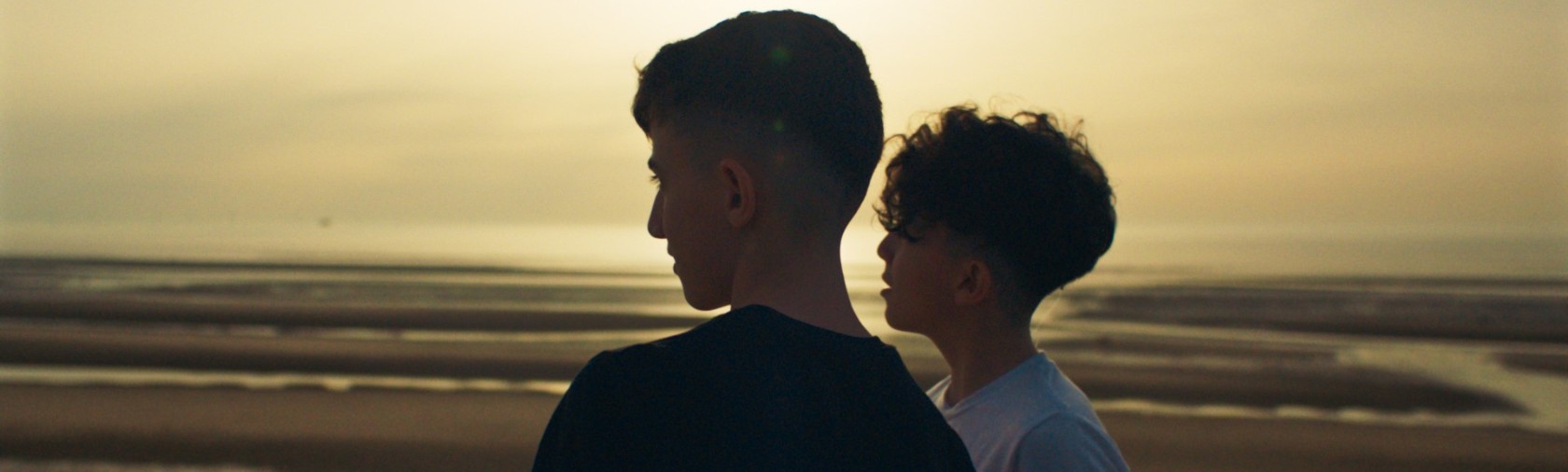 Two children looking off into the distance against a semi-lit sky