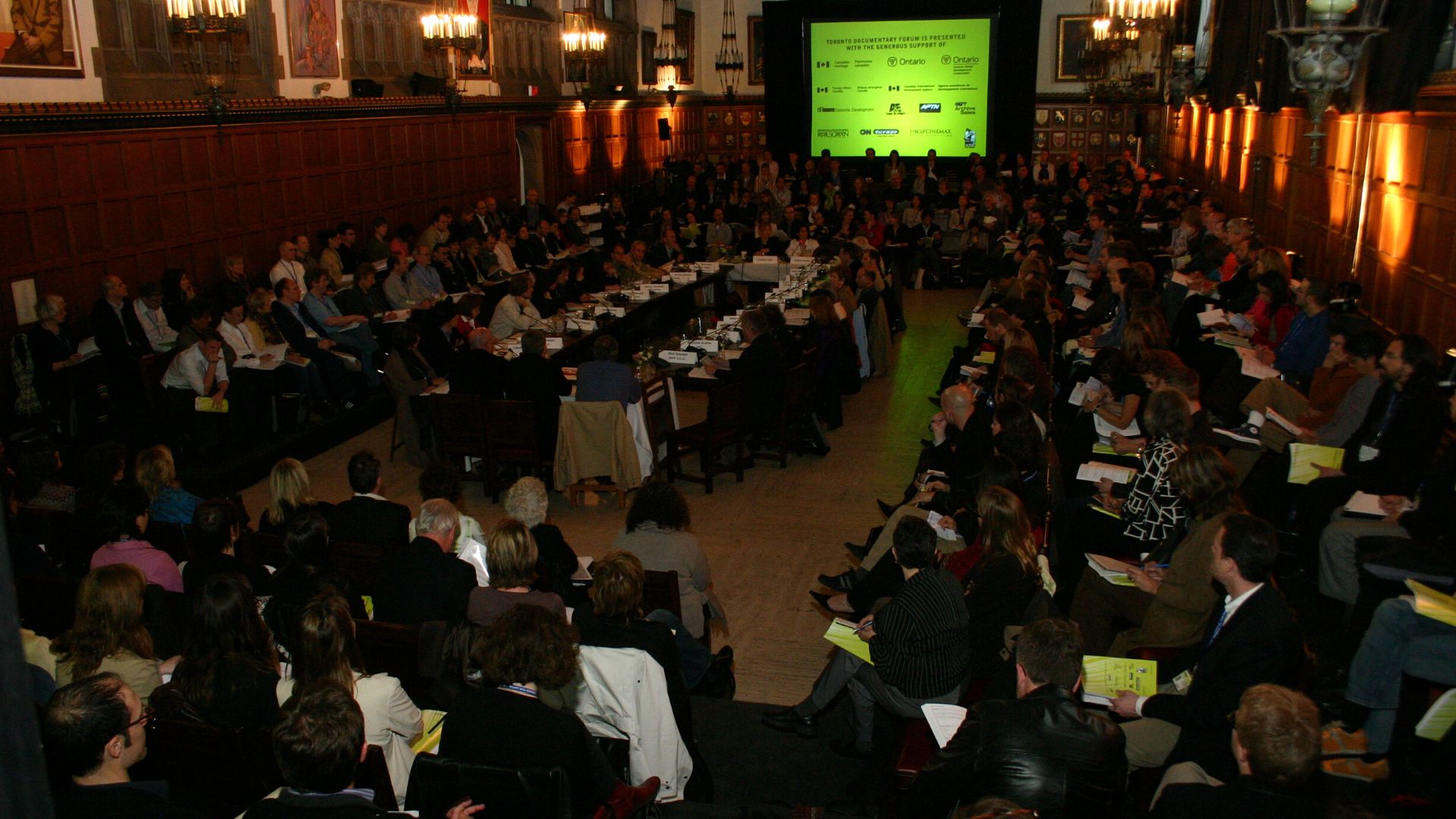 A dimly lit room full of Toronto Documentary Forum attendees seated in four continuous rows in the rectangular space. 