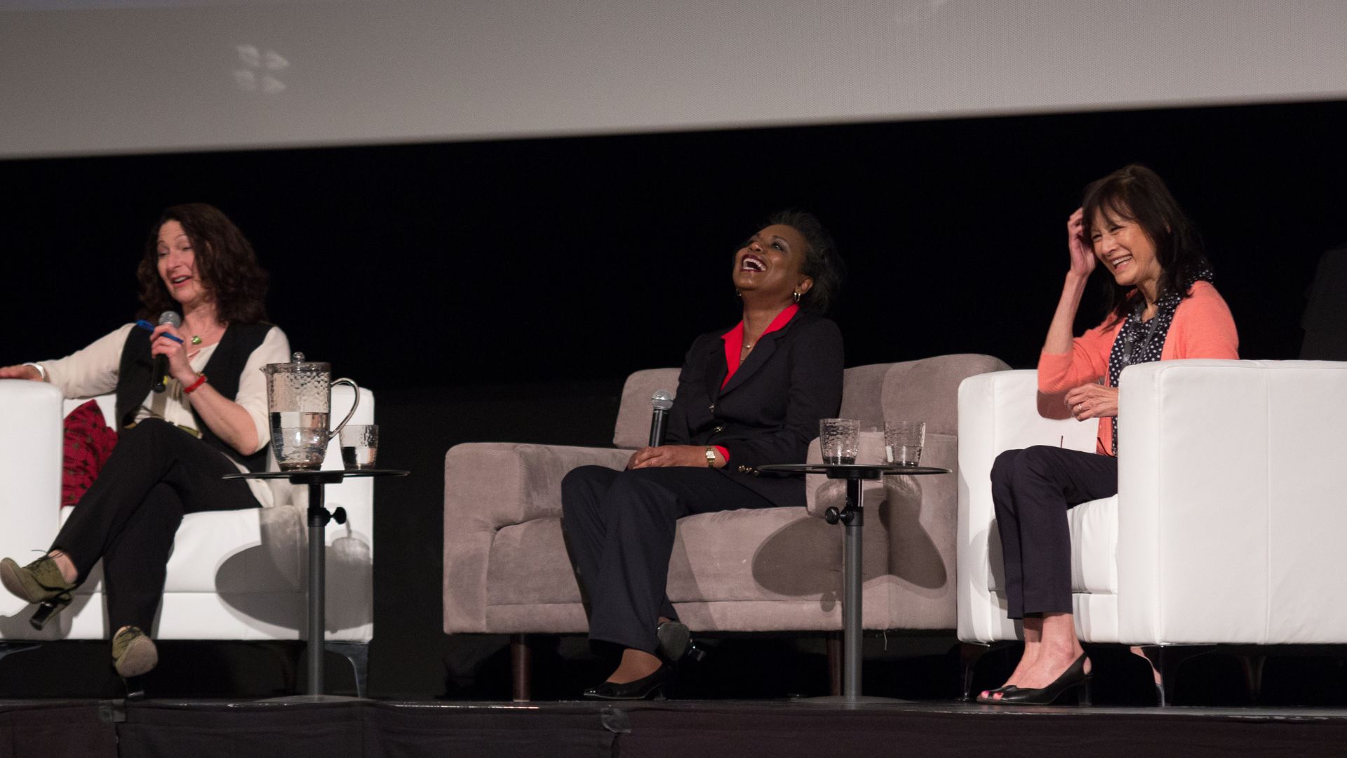 Three panelists including Anita Hill sit talking in arm chairs on an indoor stage.